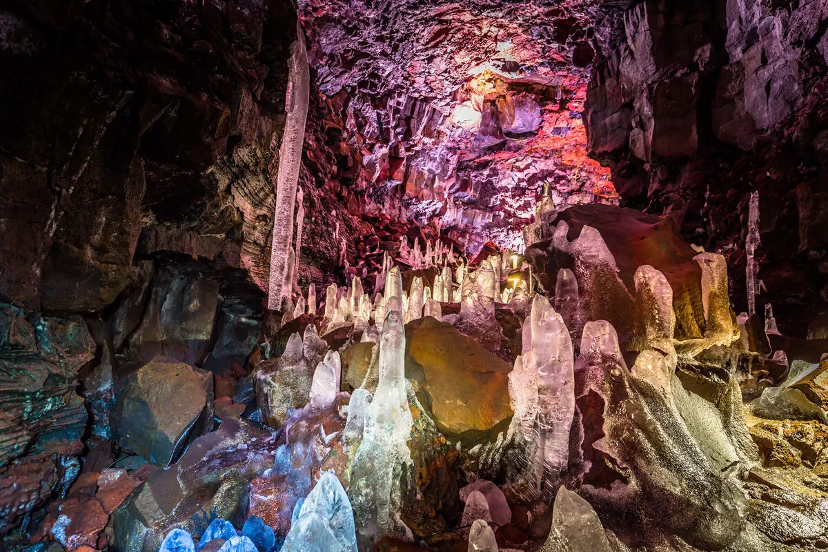 Close-up of icicle-like ice formations glowing blue and pink inside the lava tube