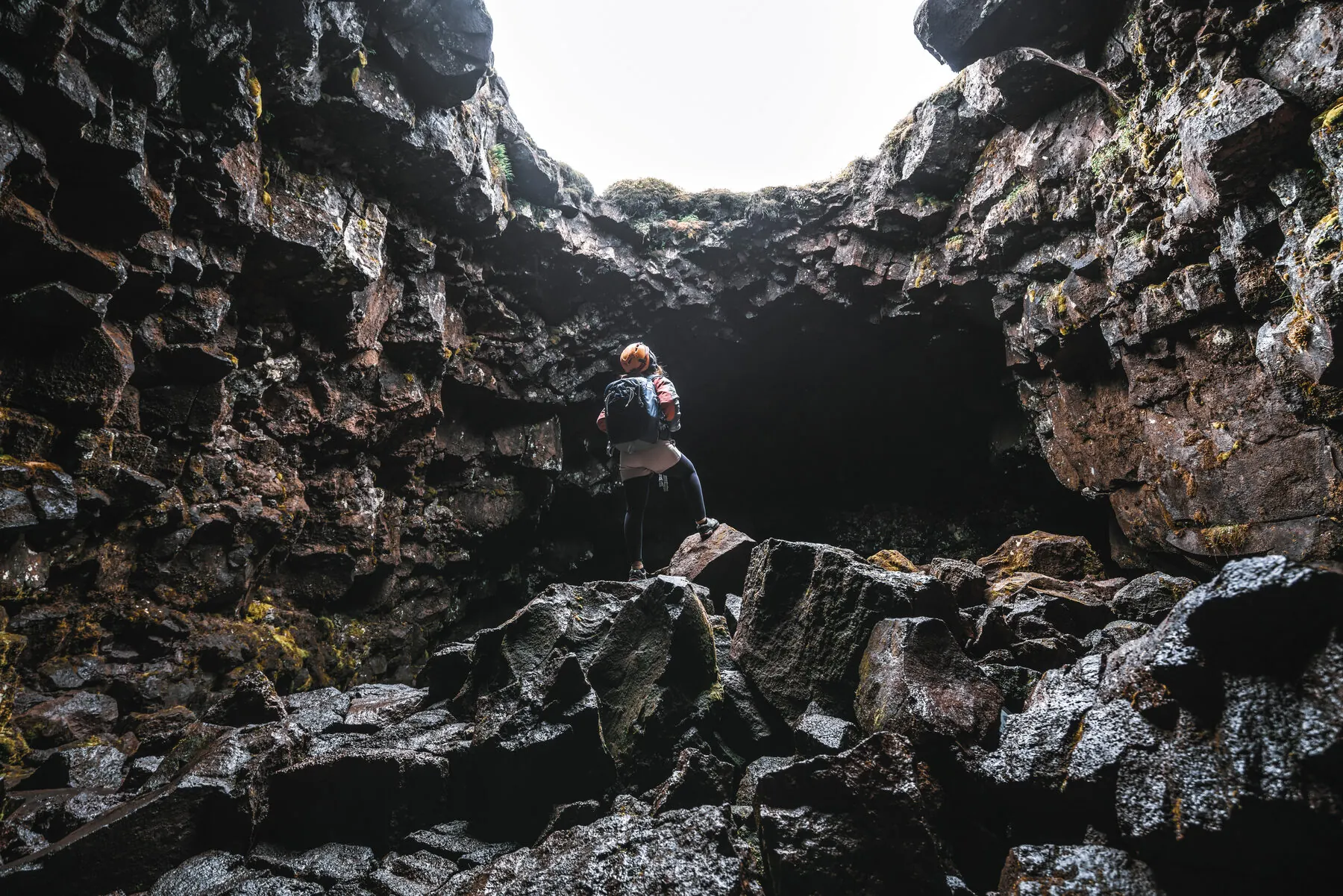 A visitor stands on rocks looking up at a shaft of daylight through a collapsed section of the tunnel roof