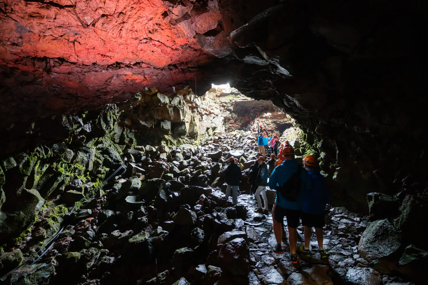 A small guided group walks along a lit boardwalk deep inside the lava tunnel