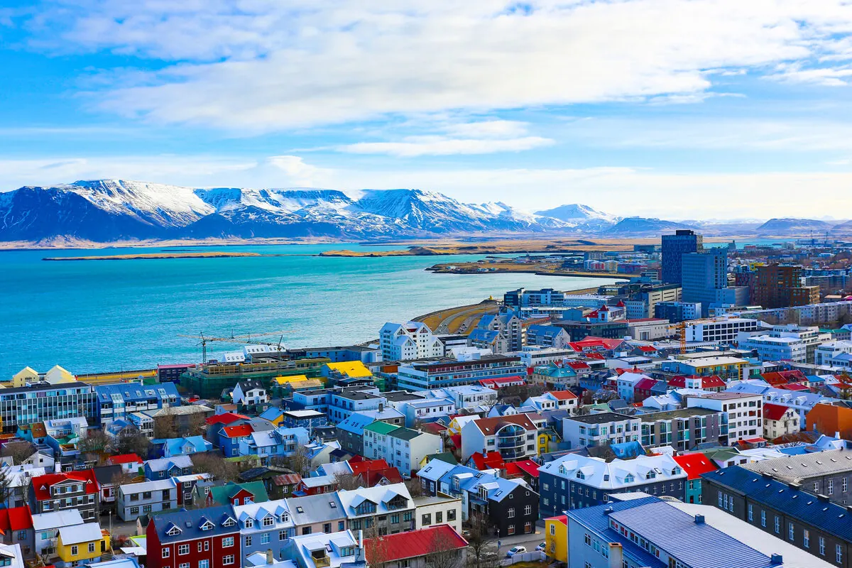 Aerial view of Reykjavík's colourful rooftops along the harbour, with snow-capped mountains across the bay