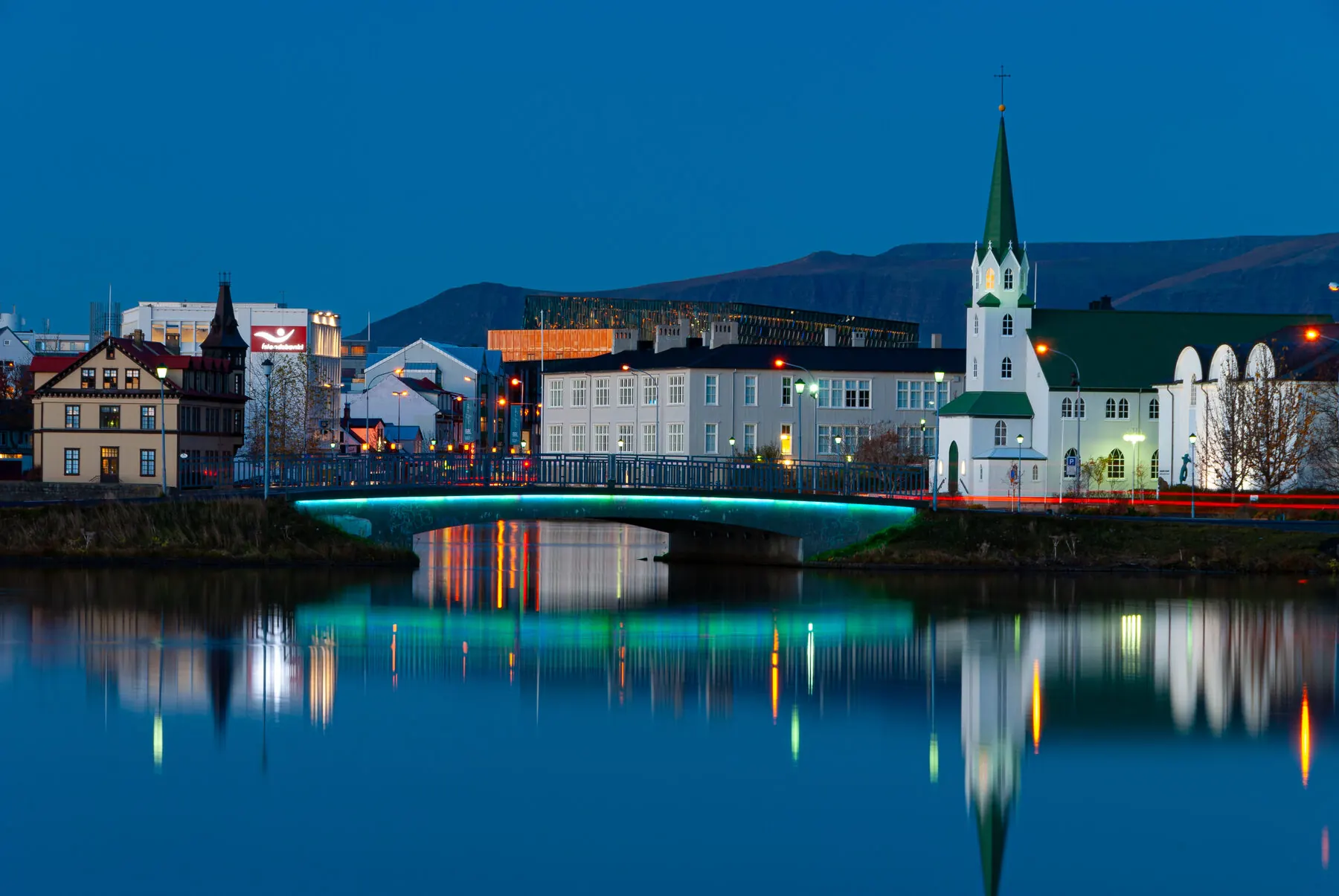Reykjavík's city pond, Tjörnin, reflecting the surrounding buildings and a footbridge at blue hour
