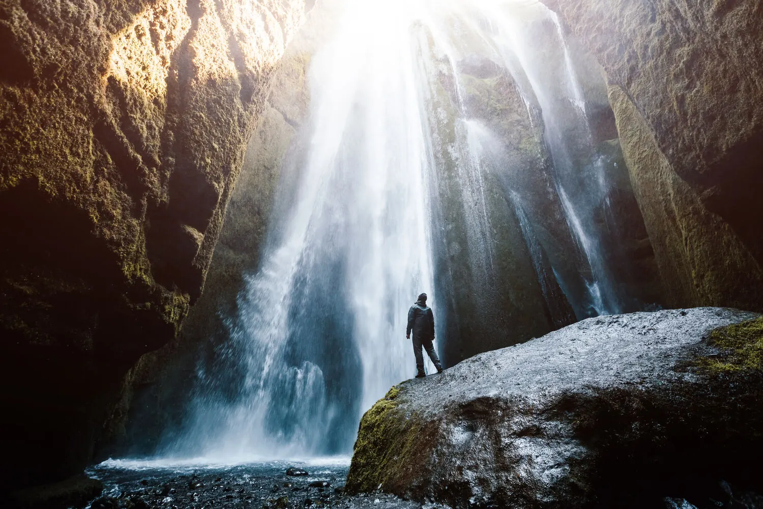 A visitor standing in the narrow canyon at the base of Gljúfrabúi waterfall