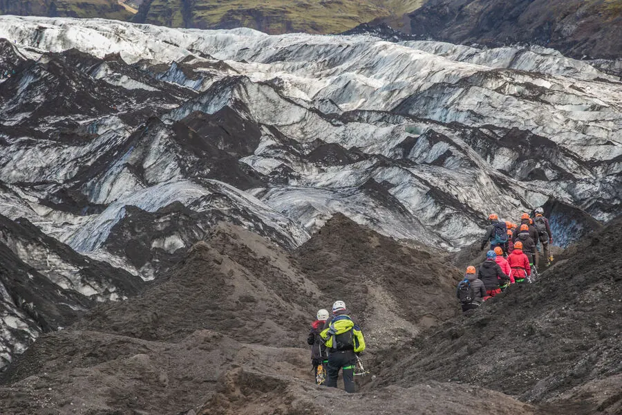 A roped line of hikers in helmets and crampons crossing a crevassed glacier in Iceland