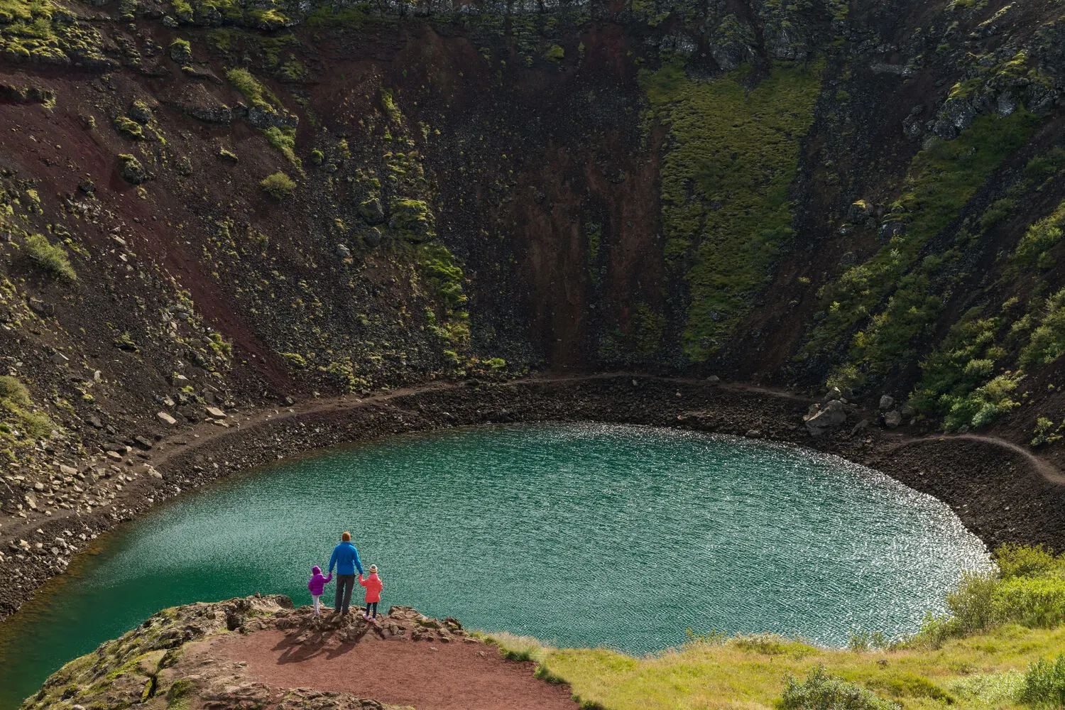 Visitors standing at the rim of Kerið crater overlooking the turquoise lake below