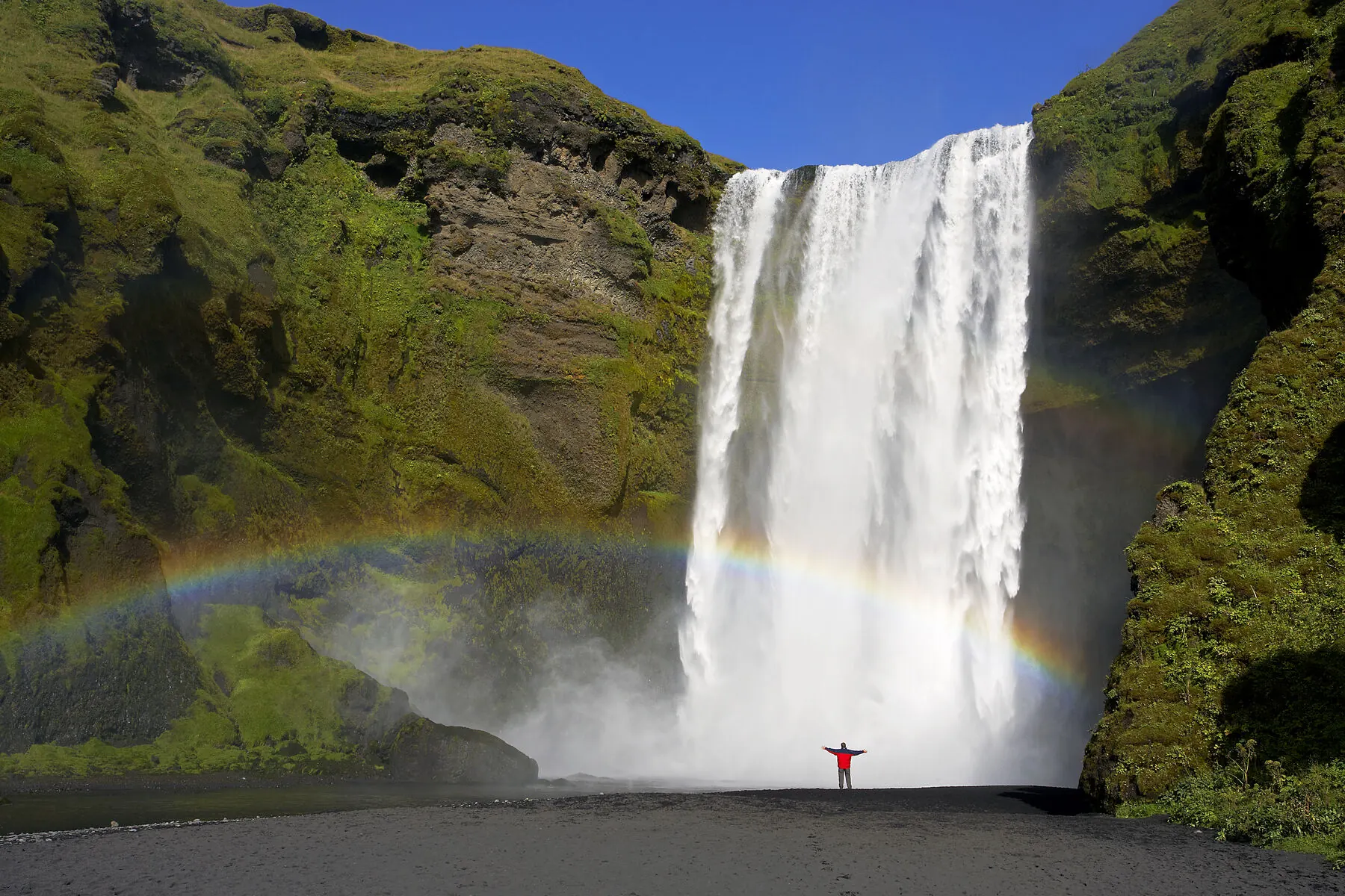 Der Wasserfall Skógafoss mit einem leuchtenden Regenbogen in der Gischt
