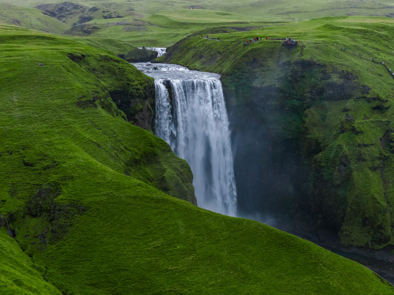 Luftaufnahme des Wasserfalls Skógafoss mit Besuchern an der Aussichtsplattform