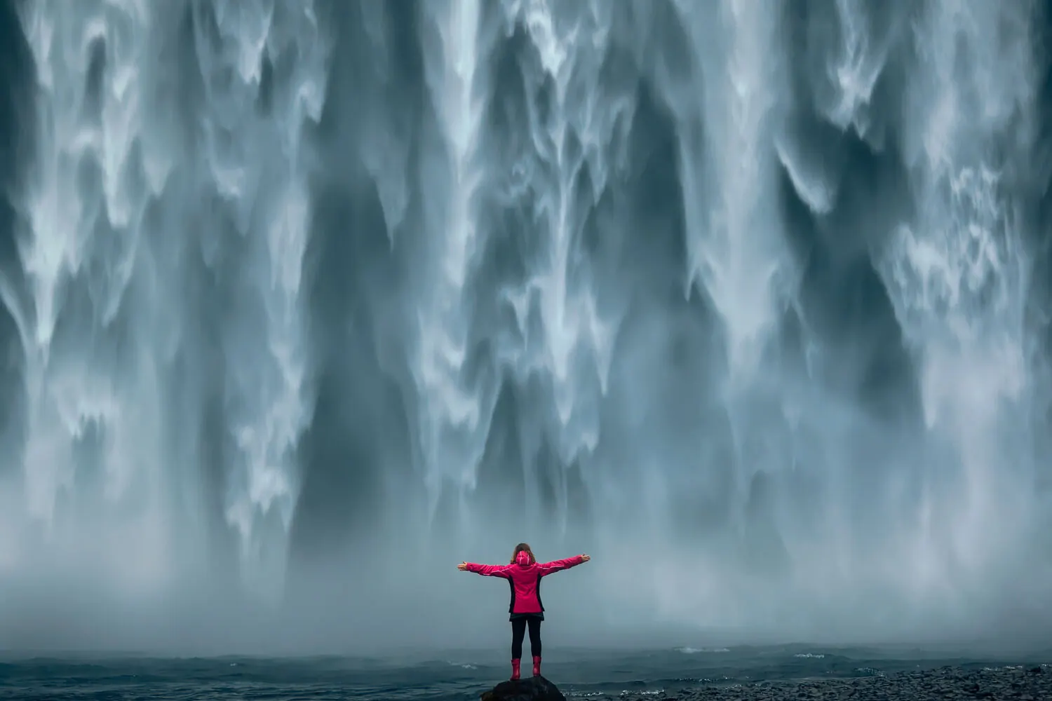 Eine Besucherin in heller Jacke nahe am Fuß des Wasserfalls Skógafoss