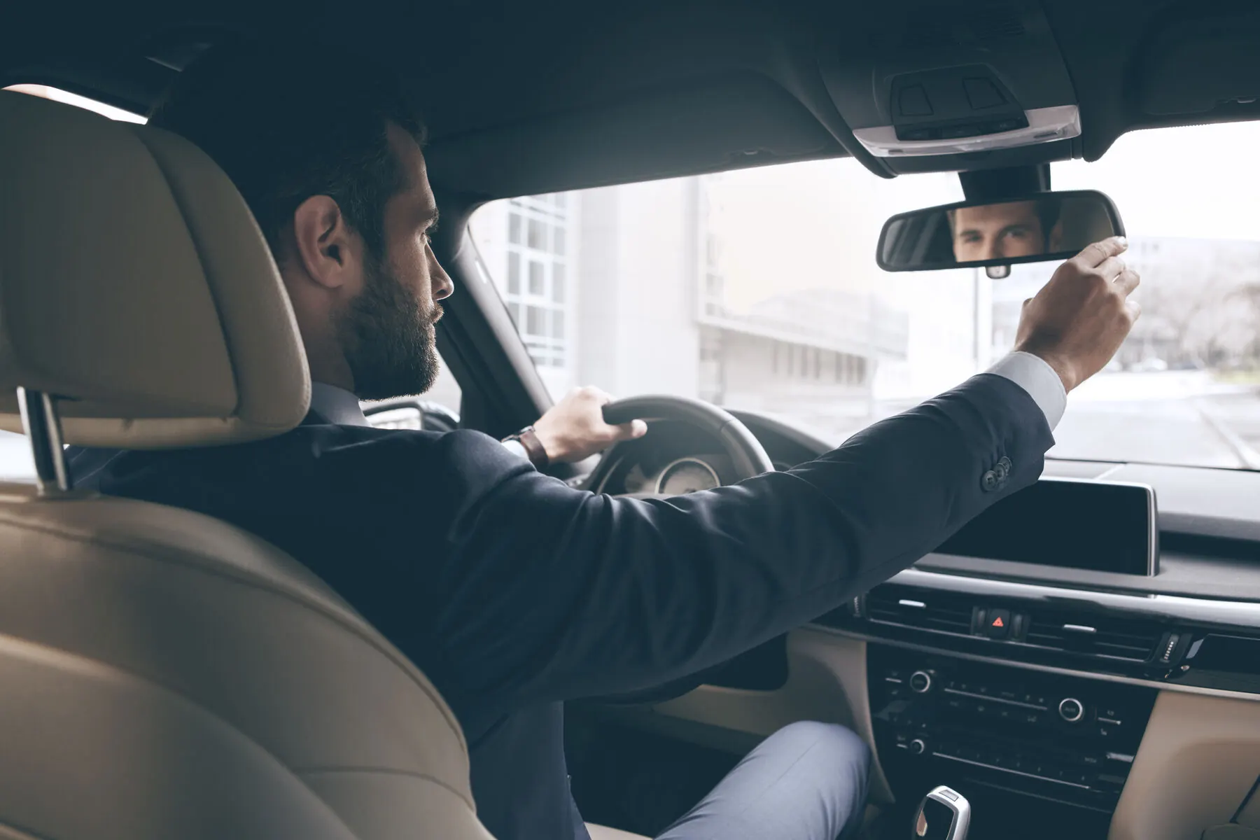 A driver in a suit adjusting the rearview mirror of a premium vehicle
