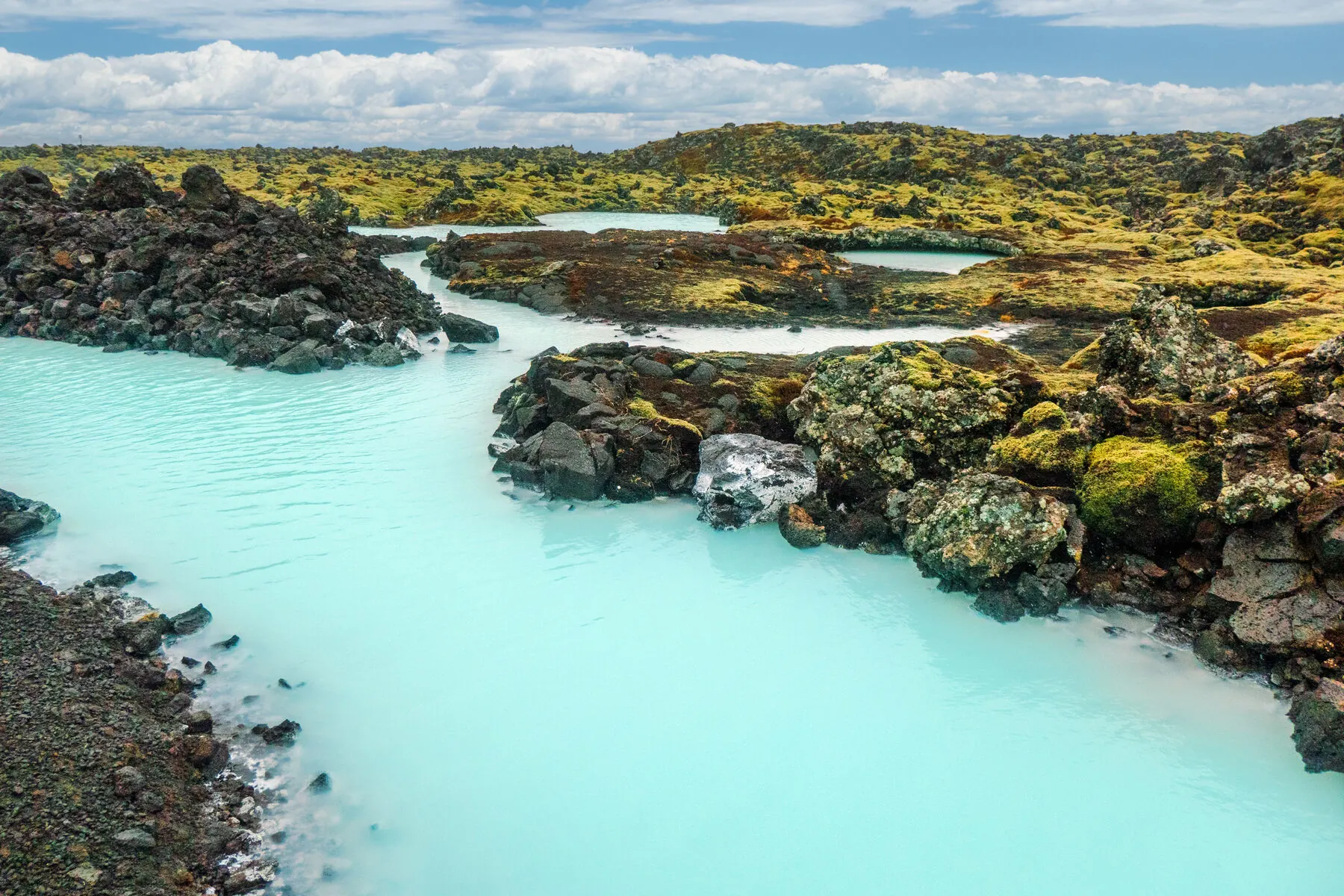 Warm turquoise geothermal water curving between dark rock walls